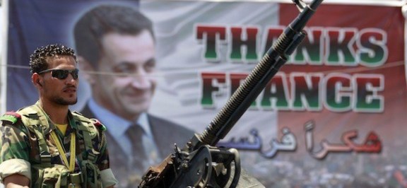 A rebel fighter mans an anti-aircraft machine gun atop a pick-up truck in front of a poster of France's President Nicolas Sarkozy in Benghazi